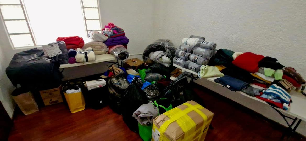 Ropa, frazadas y cobijas donadas, acomodadas sobre mesas en el centro de acopio