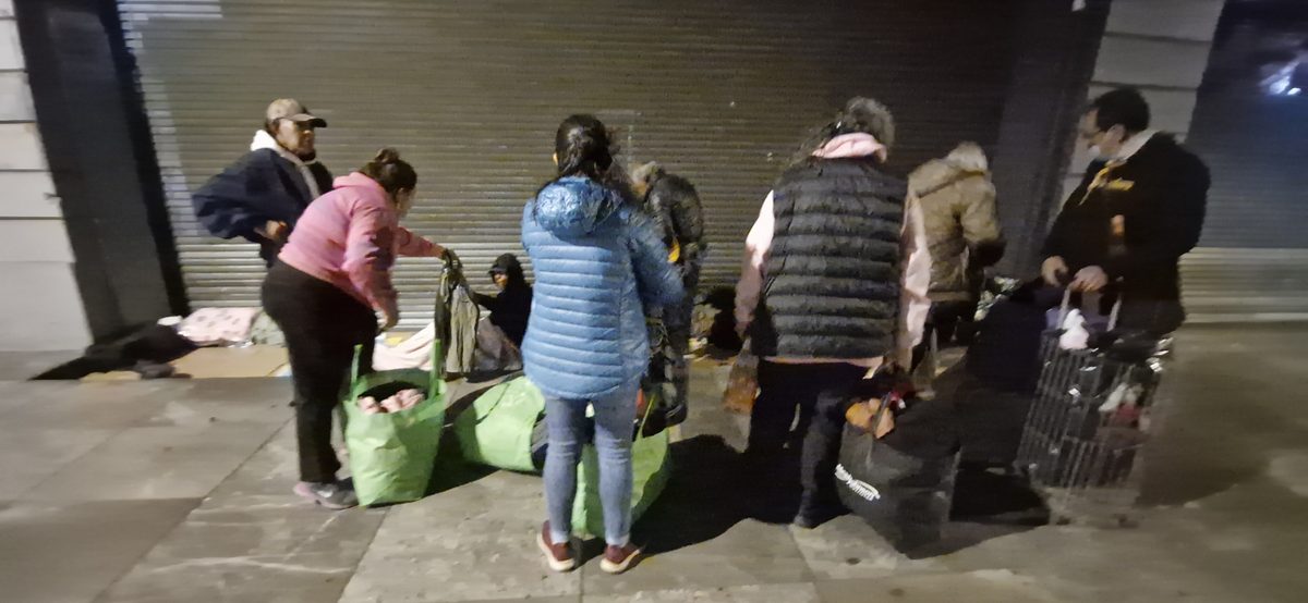 Voluntarios entregando comida y ropa abrigadora a personas en situación de calle, diciembre 2025
